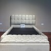 Off-white bedframe features a storage ottoman and tufted cover.