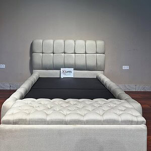 Off-white bedframe features a storage ottoman and tufted cover.